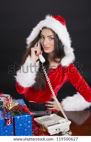Beautiful Santa girl answering the phone over dark background.