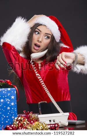 Desperate Santa girl speaking on the phone and checking the time on her wristwatch over dark background.