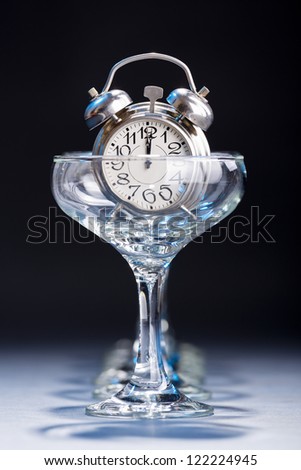 Alarm clock in an empty champagne glass showing twelve o\'clock hour.