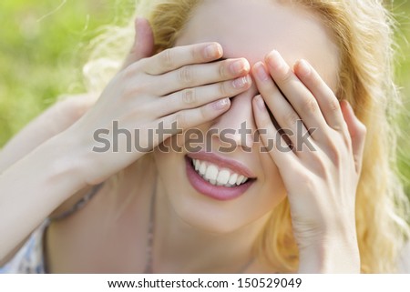 Closeup of beautiful playful smiling woman covering her eyes with both her hands. Hide-and-seek.
