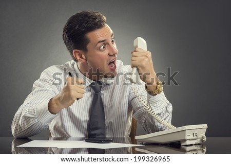 Furious businessman in white shirt and necktie having an anger outburst during a phone conversation at work. Impulsive businessman yelling and showing an enraged face grimace during phone call.