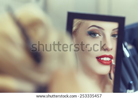 Mirror reflection of an attractive woman applying beauty makeup and cosmetics treatment. Shallow depth of field.