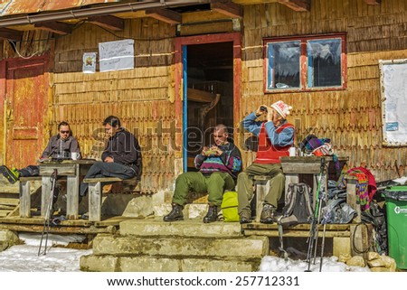 PIATRA CRAIULUI, ROMANIA - FEBRUARY 14, 2015: Unidentified tourists rest on the porch of an old lodging wooden hut at Curmatura chalet at 1470m altitude in Piatra Craiului National Park.