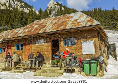PIATRA CRAIULUI, ROMANIA - FEBRUARY 14, 2015: Unidentified mountaineers rest on the porch of an old accommodation wooden hut at Curmatura chalet at 1470m altitude in Piatra Craiului National Park.
