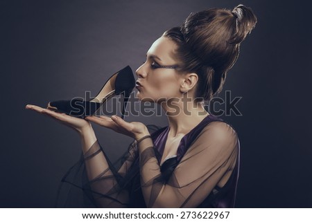 Fashion addicted sensual woman gently holding and kissing her new high heel shoe over dark background. Fashion and shopping addiction concept.