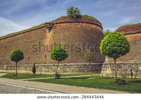 Picturesque scenery with aged medieval fortified walls,  green lawn, round trimmed ornamental trees and cobblestone alleys.
