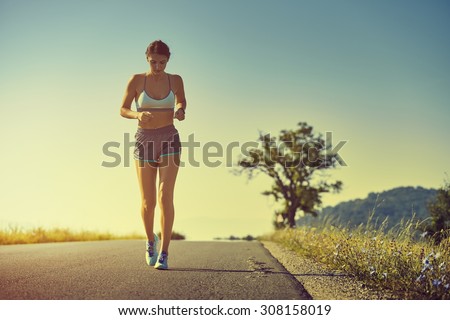 Beautiful fit woman in sport shorts running on a road at sunrise or sunset. Healthy lifestyle concept. Toned with warm instagram like filter.
