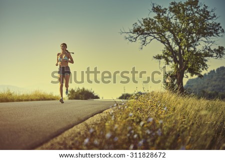 Active woman in sport shorts running on a road at sunrise or sunset. Healthy lifestyle concept. Toned with warm instagram like filter.