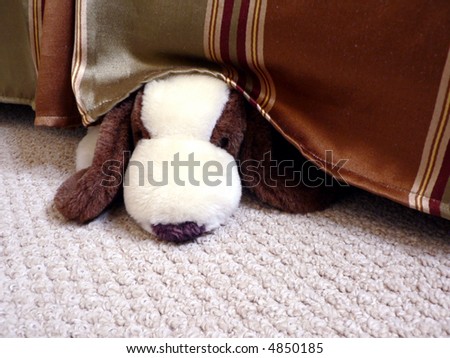 a stuffed toy dog hiding under a bed