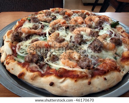 a fresh baked shrimp, sausage, spinach and onion pizza in pan ready to serve and eat
