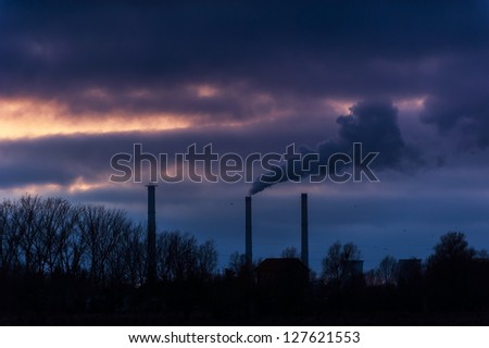 Heavy smoke spewed from coal powered plant smoke stacks under dramatic cloudy evening sky