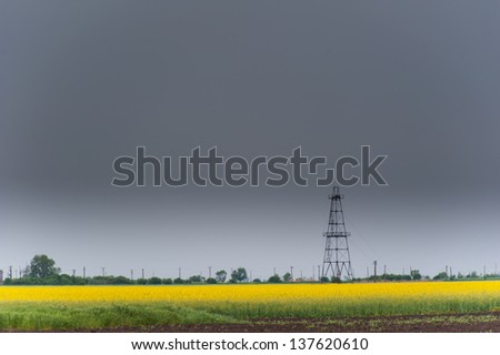 Oil and gas rig profiled over rural canola field