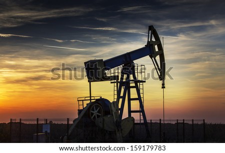 Operating oil and gas well profiled on sunset sky