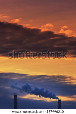 Heavy smoke spewed from coal powered plant smoke stacks under dramatic sunset