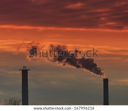 Heavy smoke spewed from coal powered plant smoke stacks under dramatic sunset