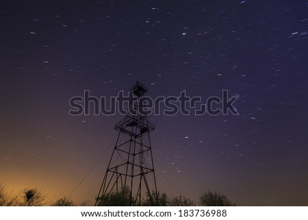 Old oil and gas rig structure, profiled on night sky, with star trails