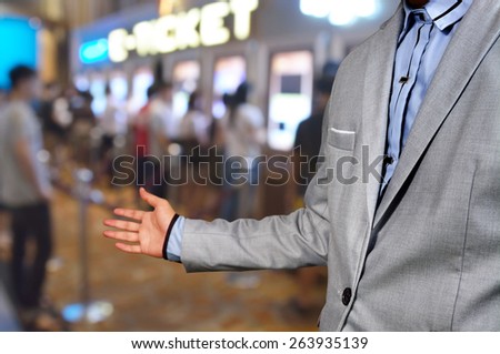 Business Man show welcome or invite gesture on Movie Ticket System Background as Entertainment business or Theatre cinema complex concept.