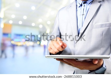 Handsome young man in shopping mall using mobile tablet.  Selective focus on Tablet in Hand.