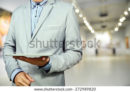 Business Man using Mobile Tablet in Gallery Art Center or Museum.  Selective Focus on Tablet and Hand.