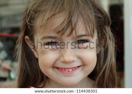 Portrait of a baby girl who smiles a toothy smile with a sparkle of happiness in her eyes.
