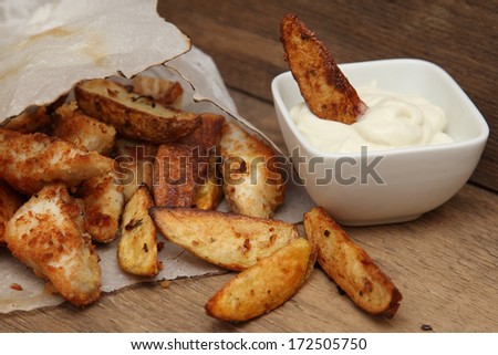 French fries potato wedges in recycled kraft paper bag on wooden old background. Fast food. Closeup. Potatoes with gravy