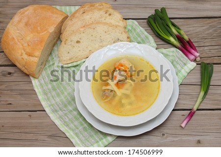 Soup with chicken leg and homemade noodles. Plate with broth. A plate of chicken soup with fresh bread and young shoots of green onions on a wooden background.