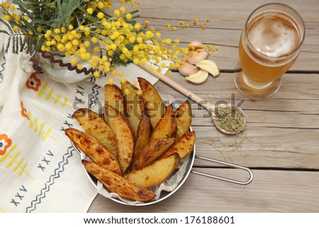 Country style potatoes. Potato wedges with slices of fried fish with rosemary, garlic and beer on a wooden background. Food style.