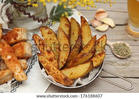 Country style potatoes. Potato wedges with slices of fried fish with rosemary, garlic and beer on a wooden background. Food style.