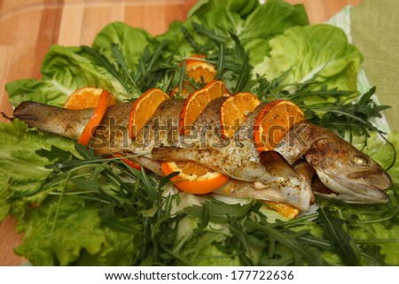 Fried fish on a bed of greens with oranges and orange slices.