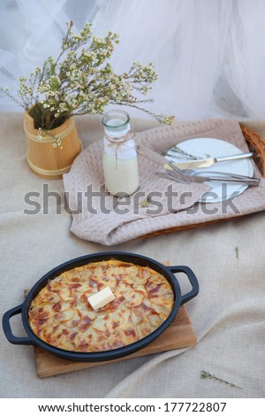 Hot baked meal with a slice of melted butter in the center. Flowers on the table, a tray of dishes and appliances, and flowers.