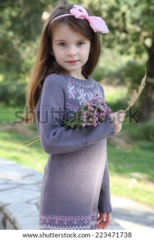 Beautiful little girl with a jug of flowers. Child with long hair. Knit dress on the little girl.