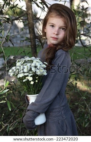 Beautiful little girl with a jug of flowers. Child with long hair. Knit dress on the little girl.