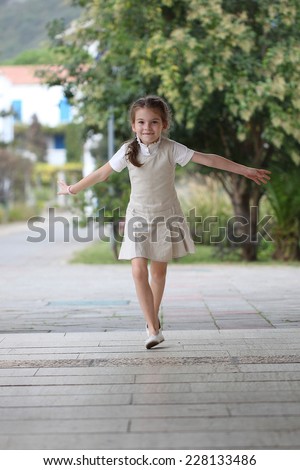Happy schoolgirl runs during recess at school. Beautiful girl is happy. Laughing kid runs and rejoices.