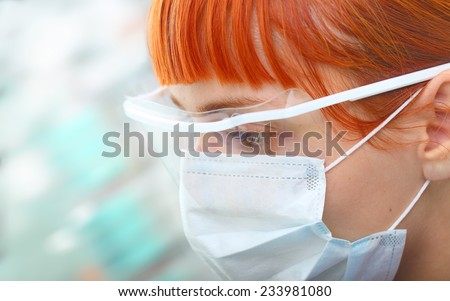 Young female scientist in protective spectacles and surgical mask attentively looks in the modern laboratory