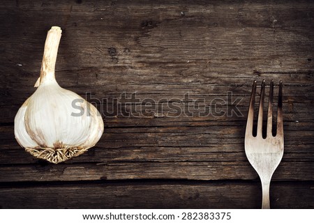 Garlic and fork on old cracked board as the food and diet concept