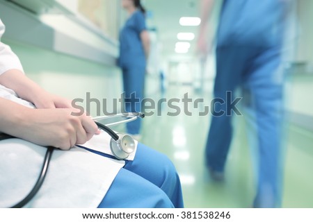 Doctor sitting alone in hospital corridor on the background of walking colleagues