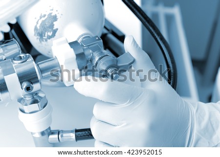 Hand on the oxygen cylinder valve in monochrome.