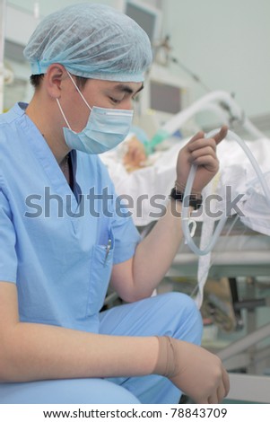 Photo a young Asian doctor in uniform; mask and cap near the bedside. Reflects the daily work in hospital;