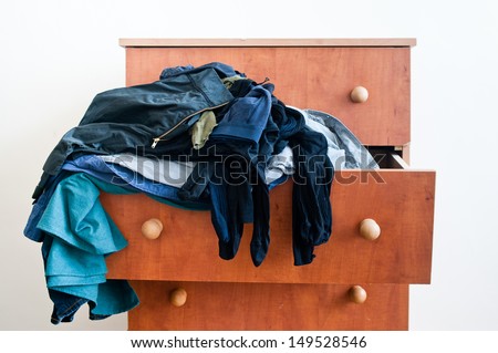 Messy brown chest of drawers with  dangling mixed man\'s and woman\'s clothes.