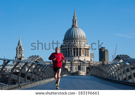 LONDON - MARCH 22: Unidentified man jogs on the Millennium Bridge with St Pauls Cathedral on the background in London on March 22, 2014. St Paul\'s is one of the top tourist attractions in London.