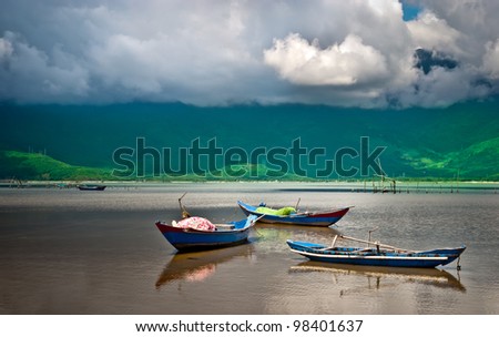 A beautiful lake view with three wooden boats under a dramatic sky