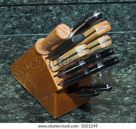 Color DSLR picture of a set of knives in a wood butcher holder. Knife collection is on a green granite countertop.
