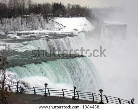 Black and white DSLR image of the water rushing over Niagara Falls, New York, in the winter.  Cold water and white snow, with spray and mist rising from cataract. Horizontal with copy space for text