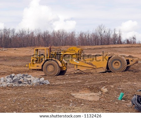 Color DSLR picture of yellow heavy equipment, an earth mover, at a construction site.  The tractor is in an open field.  Horizontal orientation with copy space for text.