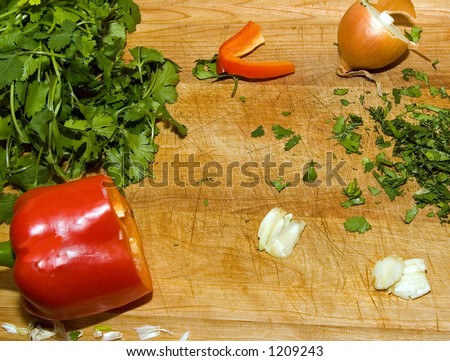 Color DSLR picture of sliced red pepper, crushed garlic, shallot, and green leafy cilantro (coriander) on wood cutting board. Healthy diet ingredients. Horizontal orientation with copy space for text