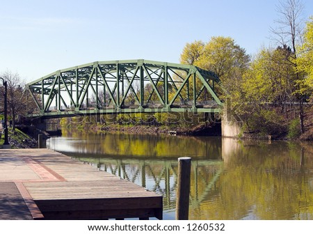 Color DSLR picture of a steel girder suspension bridge over the Erie Canal.  The sluggish flowing water is green brown.  Dock in foreground; blue sky background. Horizontal with copy space for text.