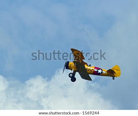 Color DSLR picture of a vintage biplane at an airshow.  Propeller airplane flying against a blue sky background with white clouds.  Horizontal orientation with copy space for text.