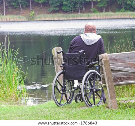 Handicapped elderly man in a wheel chair fishing at a pond