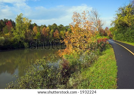 Color DSLR picture of an autumn path on the Erie Canal, Rochester, New York. Fall trees are going red, yellow, orange near the sluggish brown green water. Horizontal with copy space for text.