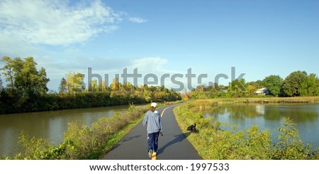 Woman walking her black labrador retriever along a path next to the Erie Canal, Rochester, New York